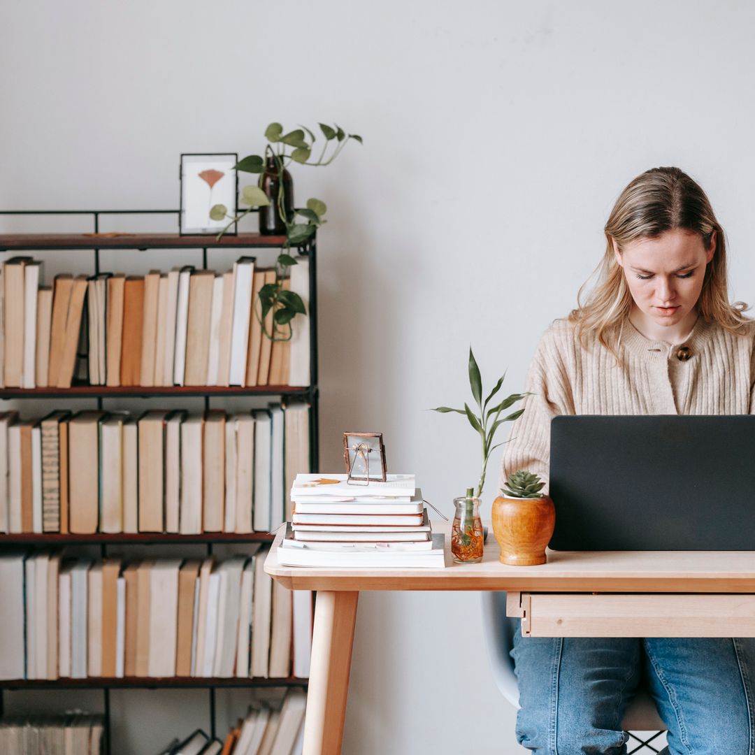 A freelancer reviewing work on a laptop at a desk with plants and books