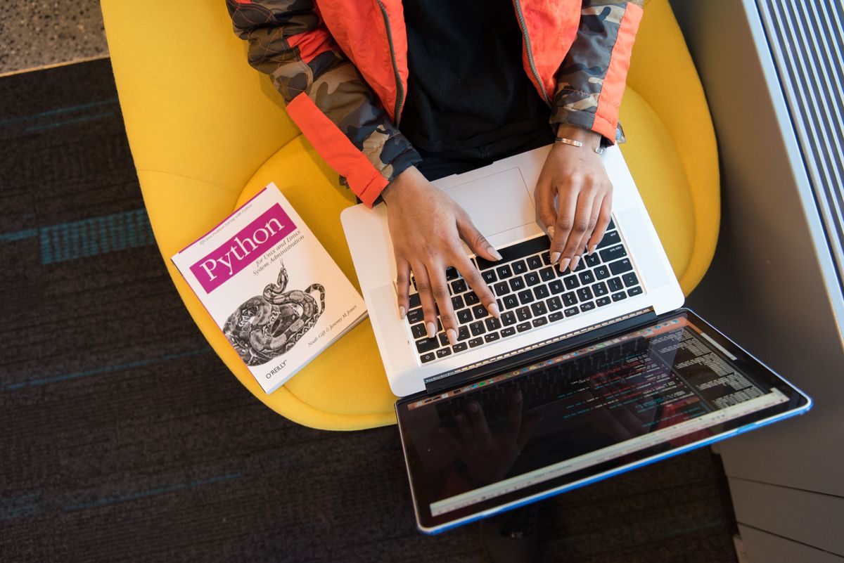 Woman programming on a laptop with a Python book beside her