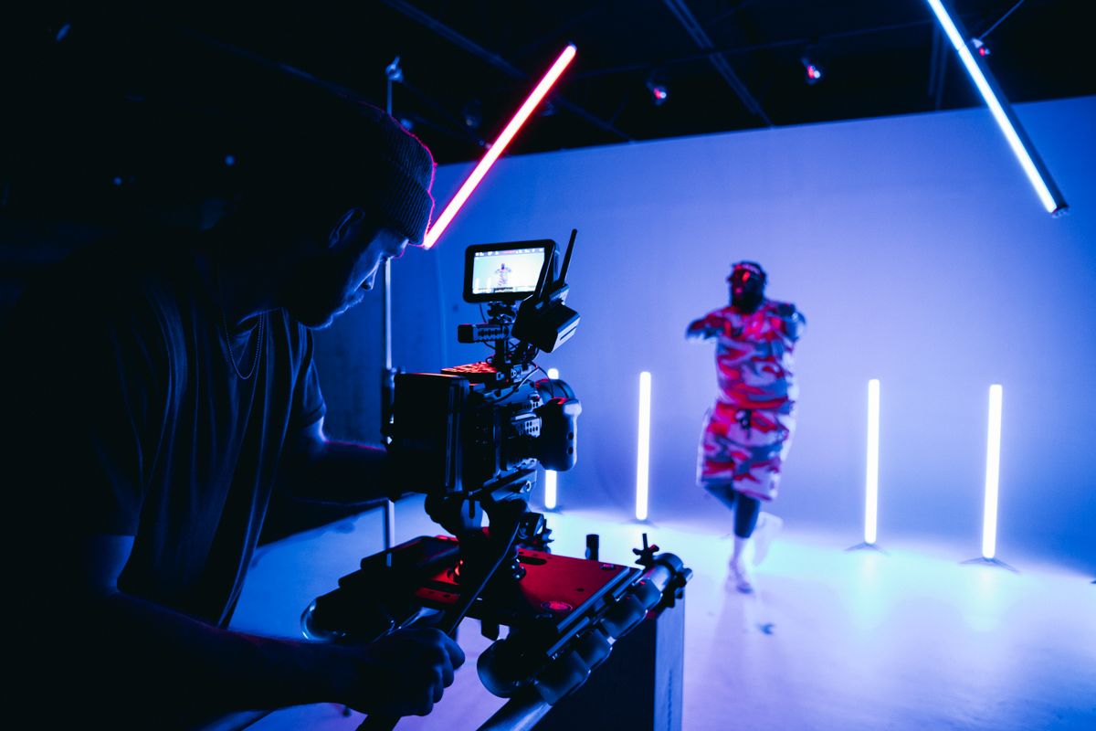 Behind the scenes of a studio video shoot with neon lights and camera crew