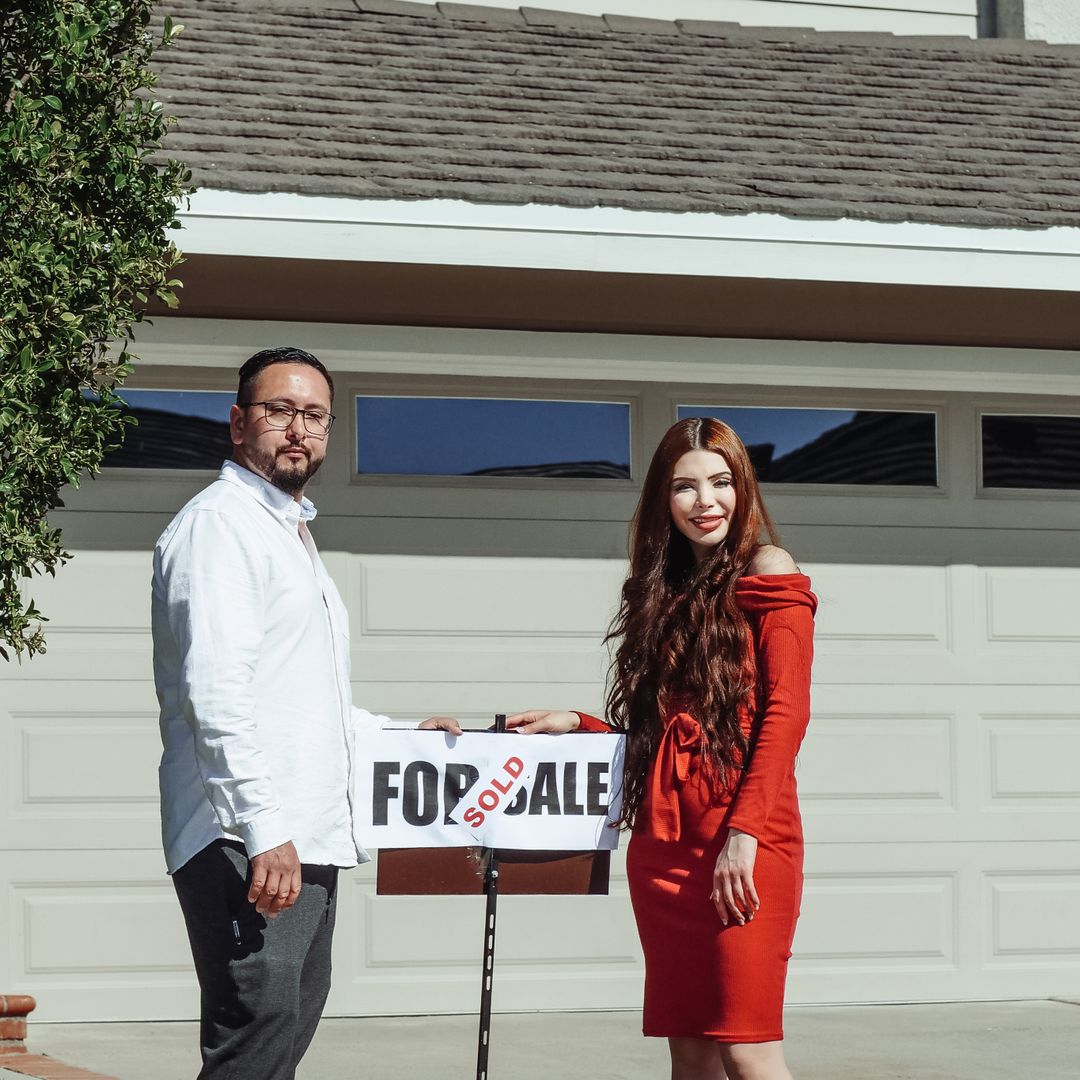 Happy couple standing outside their newly purchased home with a sold sign