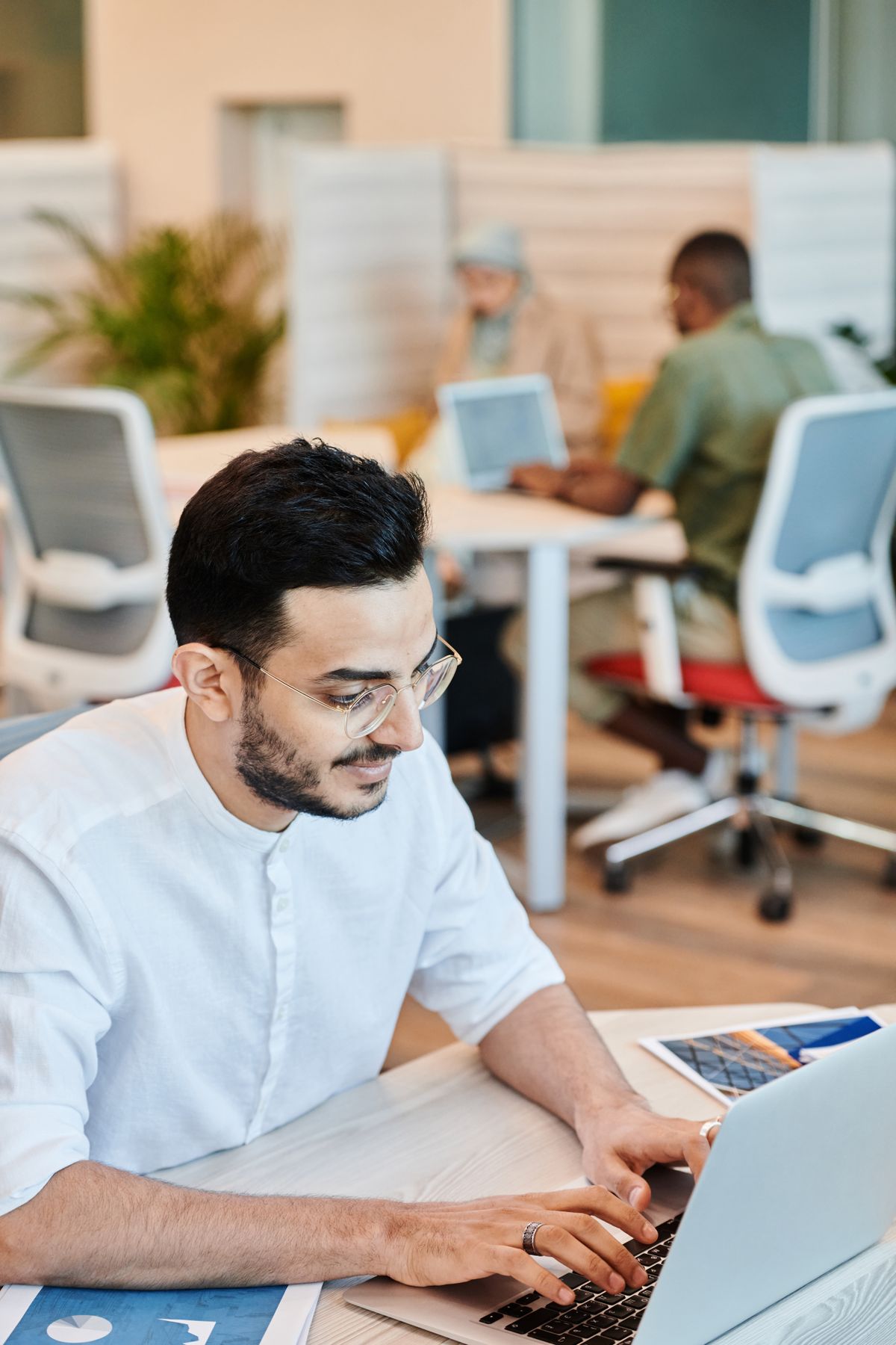 Focused salesperson typing on a laptop with colleagues working in the background