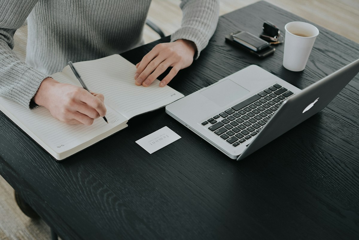 A freelance writer working on a laptop at a home desk, notebook and coffee beside the keyboard