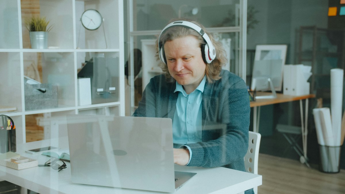 Headphones and a laptop with transcription software open, waveform visible on screen