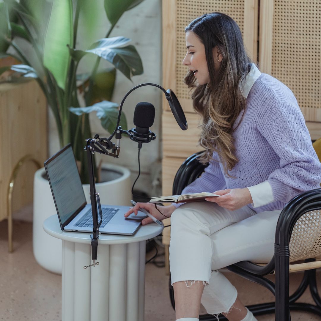 A woman recording narration into a microphone while working on a laptop