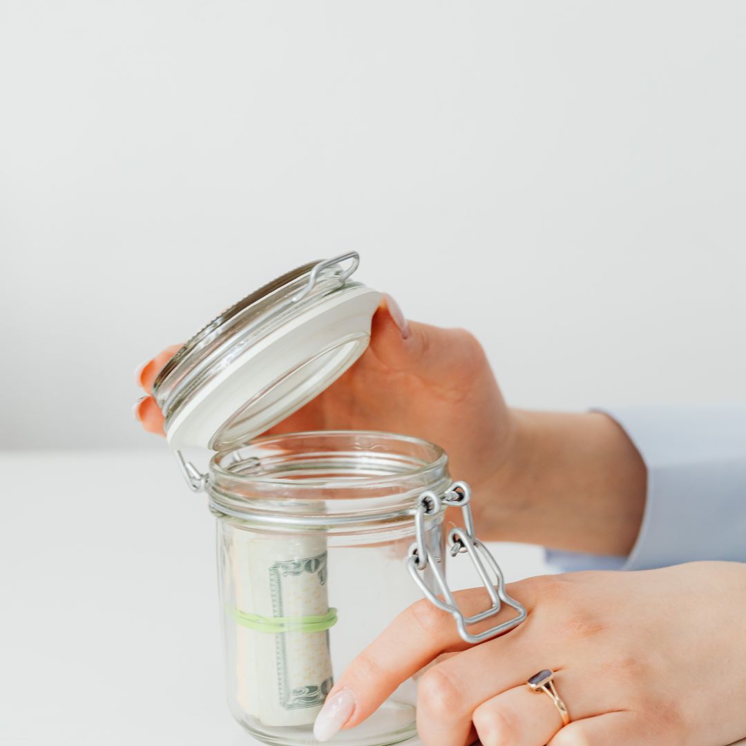 Person dropping savings into a glass money jar