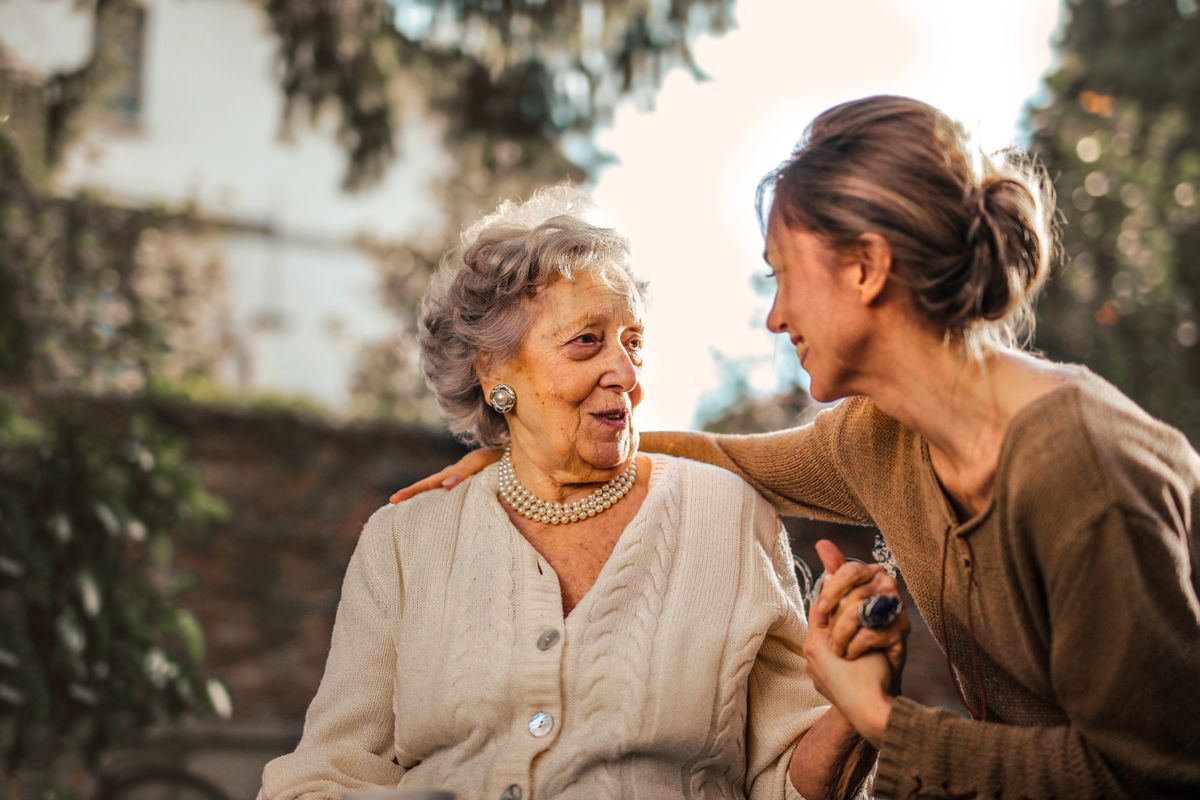 Adult daughter comforting her elderly mother outdoors, arm around her shoulder