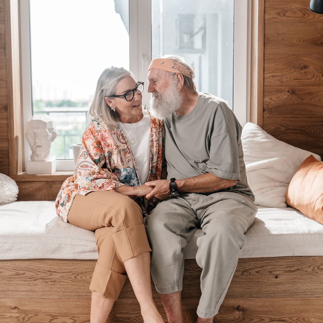 Older couple holding hands and smiling at each other while sitting together at home