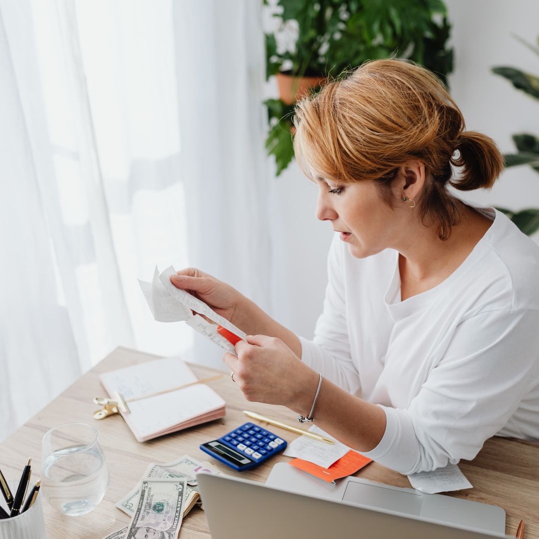 Woman managing business finances with calculator and paper receipts at a desk