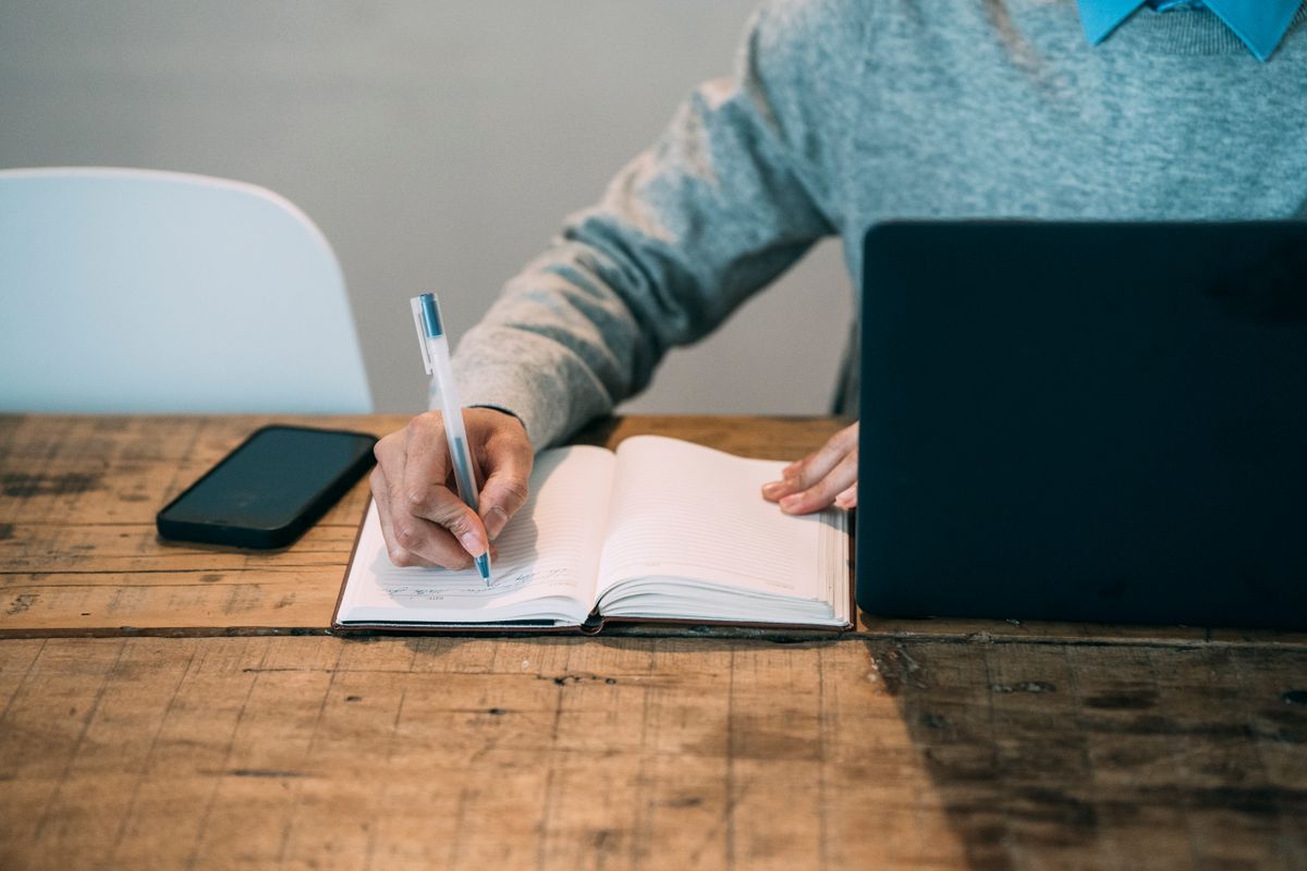 A person writing in a planner next to a laptop, designing digital products