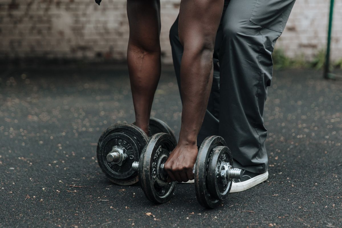 A man picking up a pair of adjustable dumbbells outdoors before a workout