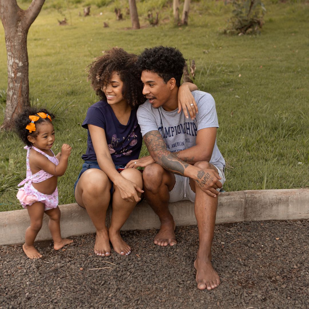 Smiling family with parents and toddler playing together on a sunny lawn