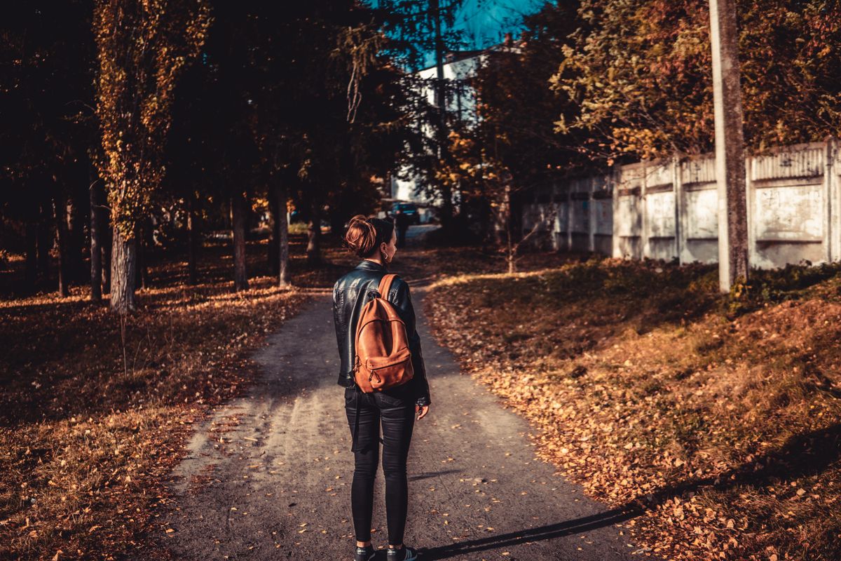 A woman with a backpack walking down an autumn park path in golden light